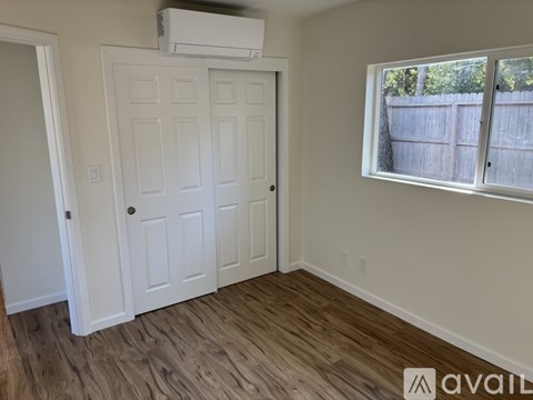 A room with a white door, a window, and a wooden floor.