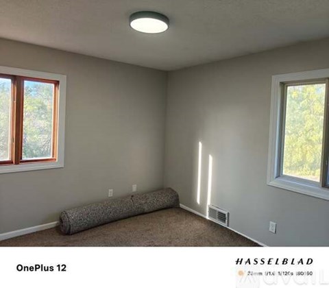 A room with a carpeted floor, a window, and a wall-mounted air conditioning unit.
