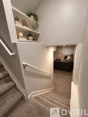 A staircase with a white railing and a living room with a couch and a plant in the background.