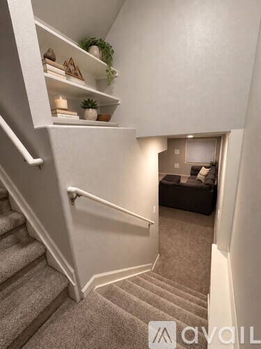 A staircase with a white railing and a living room with a couch and a plant in the background.