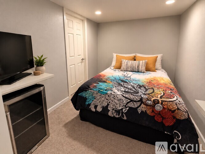 A bedroom with a bed covered in a colorful quilt and a television on a stand.