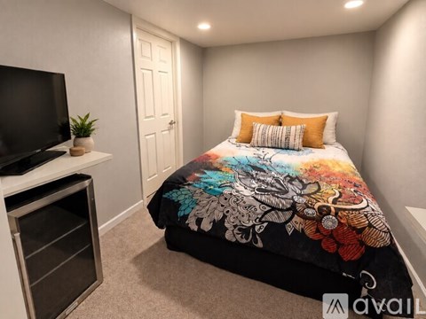 A bedroom with a bed covered in a colorful quilt and a television on a stand.