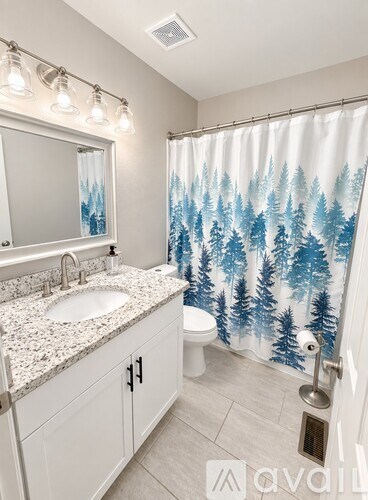A bathroom with a white sink and a shower curtain with trees on it.