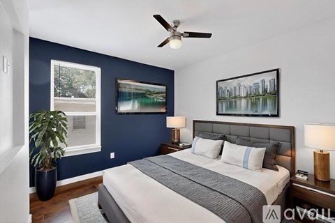 A bedroom with a bed, a ceiling fan, and a painting on the wall.