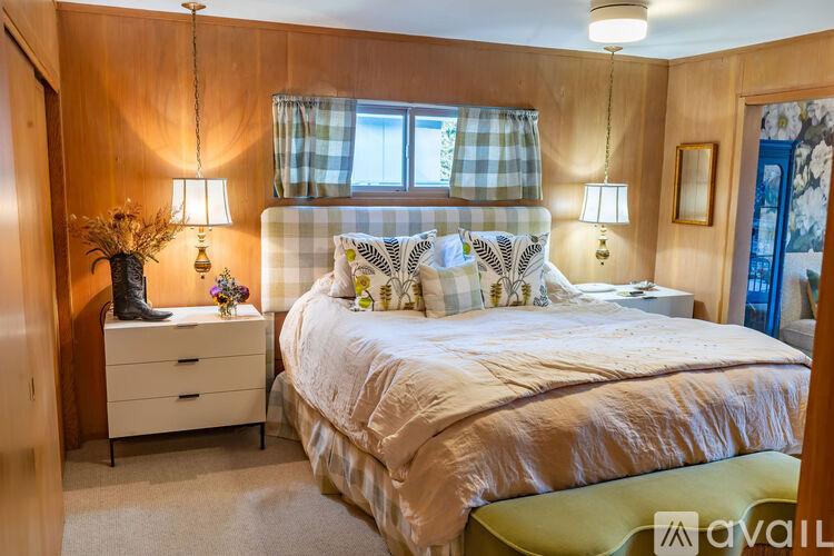A bedroom with a large bed, a nightstand with a lamp, and a window with curtains.