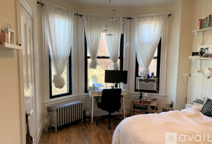 A bedroom with a bed, desk, and window with curtains.