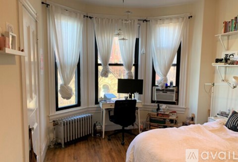 A bedroom with a bed, desk, and window with curtains.