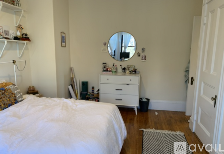 A white bedroom with a round mirror and a white dresser.