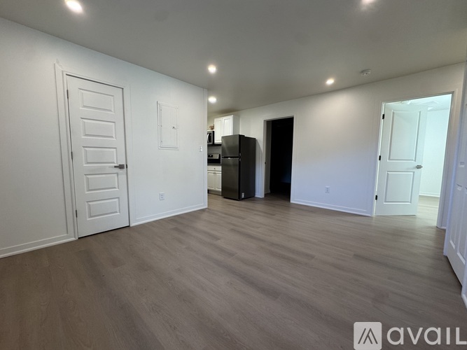 A spacious room with wooden flooring and white walls, featuring a white door and a black cabinet.