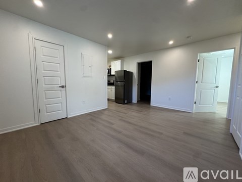 A spacious room with wooden flooring and white walls, featuring a white door and a black cabinet.
