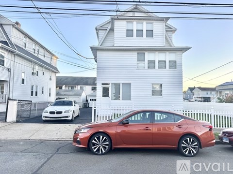 A red car is parked in front of a white house.