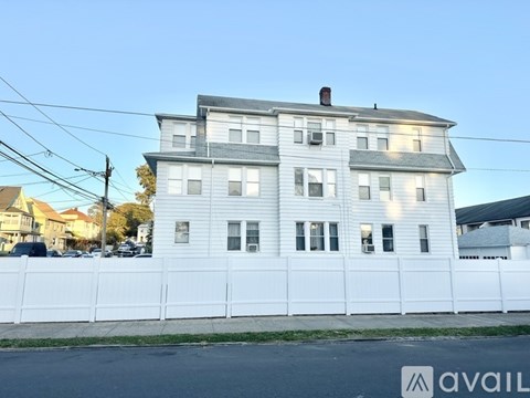 A white house with a grey roof and a white fence in front of it.