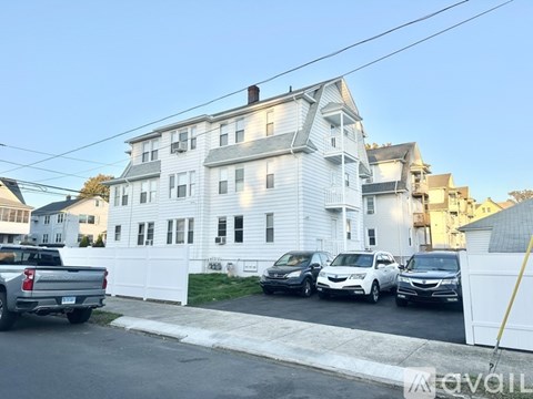 A white two-story house with a garage and a driveway with cars parked in front.