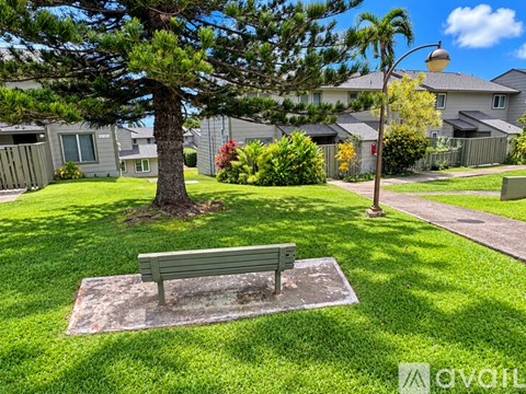 A bench sits in the middle of a grassy area with a tree and a lamp post in the background.