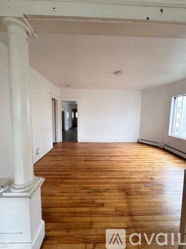 A large empty room with wooden floors and white columns.
