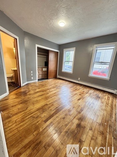 A room with wooden flooring and a window with a view of a red car.