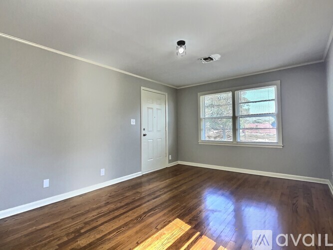 A room with wooden floors and a window showing a view of trees and a building outside.