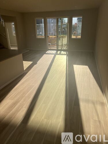 A room with wooden flooring and a large window letting in sunlight.