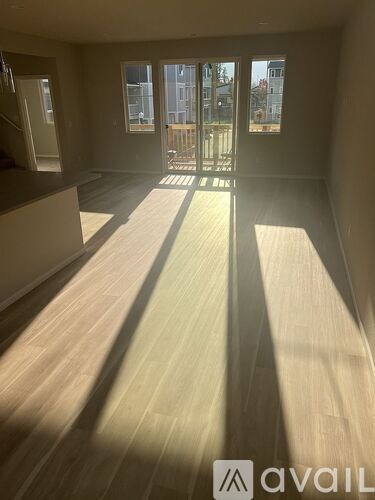 A room with wooden flooring and a large window letting in sunlight.