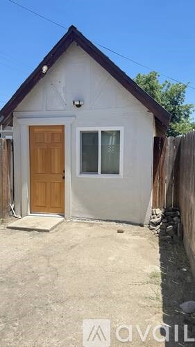 A small white house with a brown door and a window is for sale.
