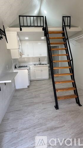 A staircase with a wooden handrail and black balusters leads up to a kitchen area.