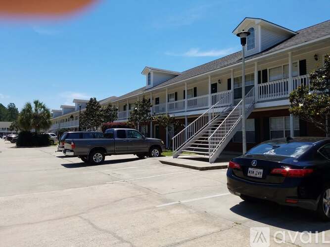 A black car is parked in a parking lot in front of a white building with a balcony.
