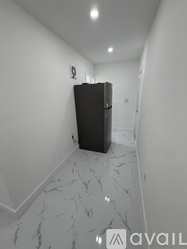 A black fridge in a white room with marble flooring.