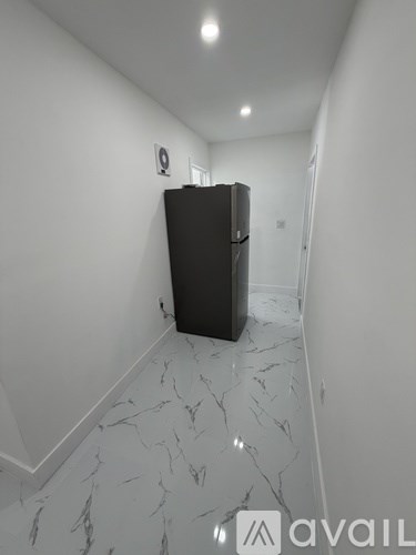 A black fridge in a white room with marble flooring.