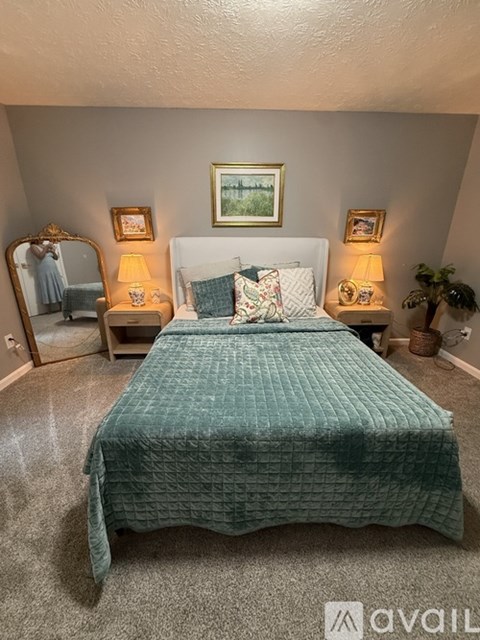 A bedroom with a bed covered in a green quilted bedspread.
