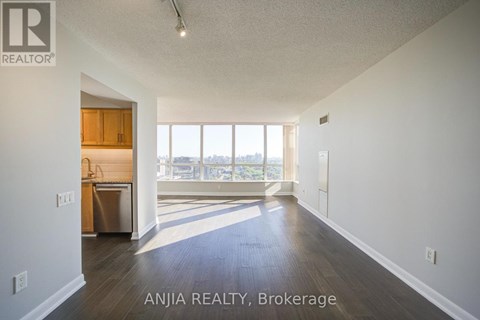 A spacious room with wood flooring and a kitchen area in the background.