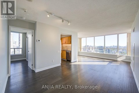 A spacious room with wood flooring and a large window overlooking the city.