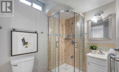 A bathroom with a white toilet, a sink, a mirror, and a shower with a glass door.