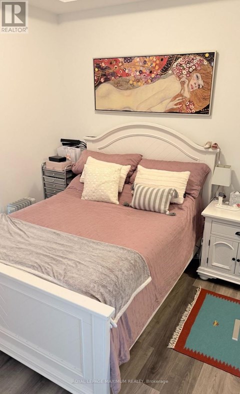 A bedroom with a bed, nightstand, and a painting on the wall.