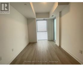 A spacious room with wooden flooring and a large window with blinds.