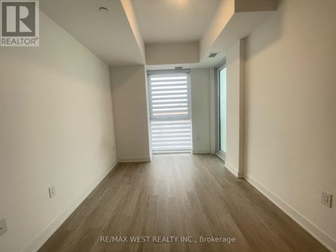 A spacious room with wooden flooring and a large window with blinds.