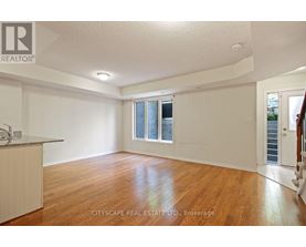 A spacious room with wooden floors and white walls, with a window and a door visible.