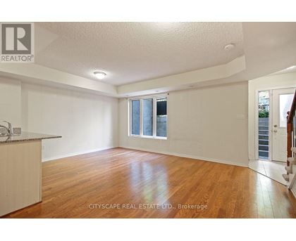 A spacious room with wooden floors and white walls, with a window and a door visible.