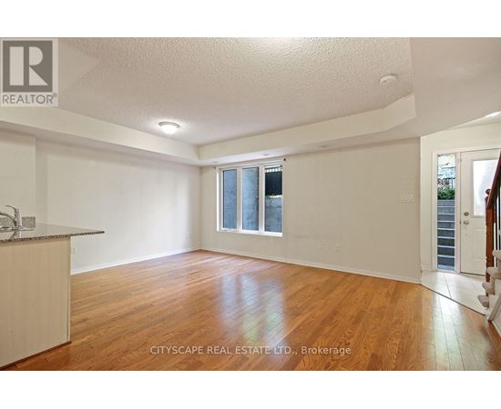 A spacious room with wooden floors and white walls, with a window and a door visible.