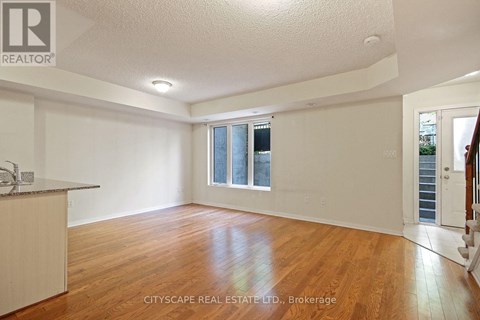 A spacious room with wooden floors and white walls, with a window and a door visible.