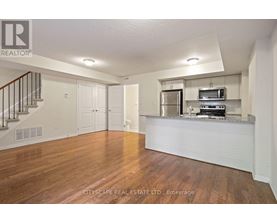 A spacious living room with wood flooring and a staircase on the left side.