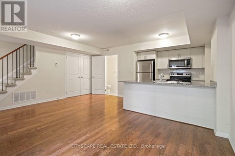 A spacious living room with wood flooring and a staircase on the left side.