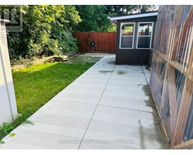 A concrete walkway leads to a small black building with a glass door.