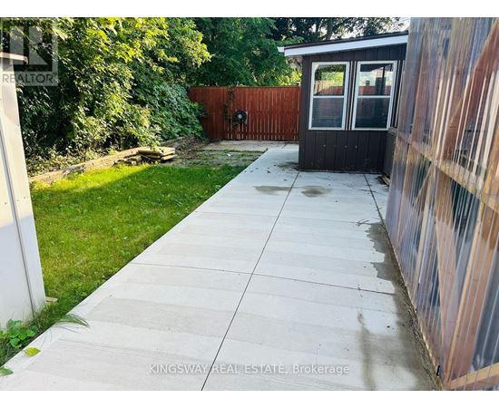A concrete walkway leads to a small black building with a glass door.
