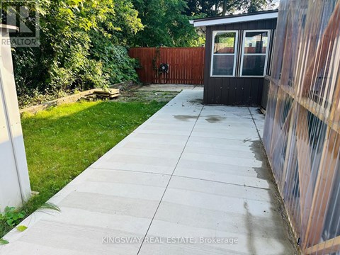 A concrete walkway leads to a small black building with a glass door.