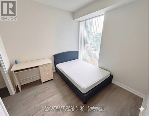 A bedroom with a bed, desk, and window.