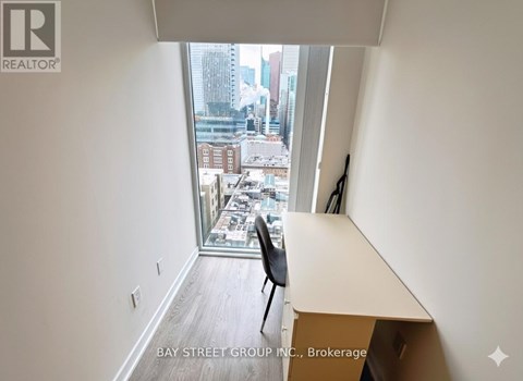 A room with a desk and a chair with a window that has a view of the city.