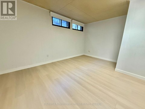 A room with wooden flooring and two windows.