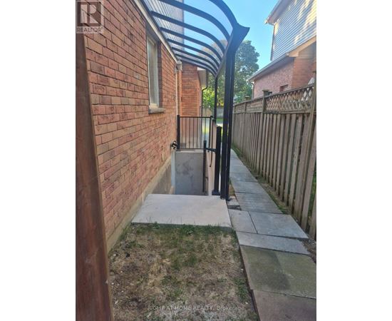 A brick wall with a metal gate and a concrete pathway leading to a small door.