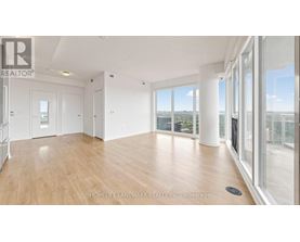 A spacious room with wooden flooring and large windows overlooking a cityscape.