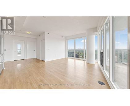 A spacious room with wooden flooring and large windows overlooking a cityscape.